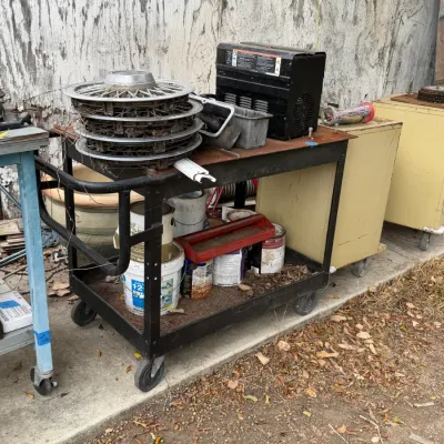Sale Photo Thumbnail #23: Black metal two-shelf rolling utility cart loaded with hubcaps, paint cans, and shop supplies.