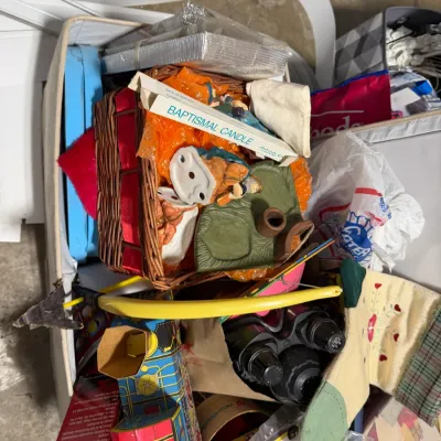 Sale Photo Thumbnail #14: Storage bin filled with various household items, religious collectibles, a baptismal candle, Christmas decorations, and vintage toys.