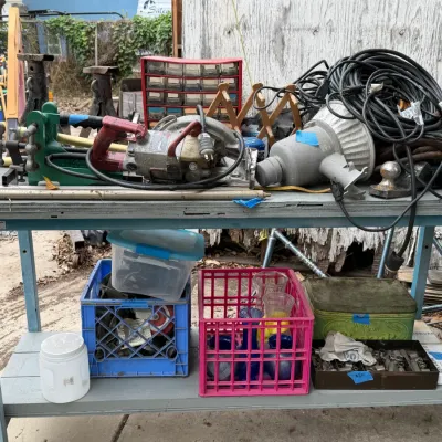 Sale Photo Thumbnail #20: Blue two-tiered metal workbench loaded with assorted power tools, extension cords, hardware bins, and plastic crates containing glassware and small parts.