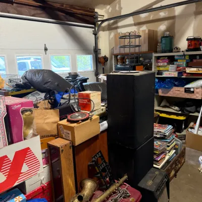 Sale Photo Thumbnail #7: Sale area featuring a brass saxophone needing repair, audio speakers, a small guitar amplifier, and shelves filled with board games and household items.