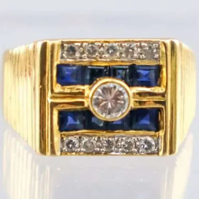 Sale Photo Thumbnail #9: Men's yellow gold geometric ring featuring a central bezel-set round diamond, flanked by channel-set square sapphires and rows of accent diamonds.