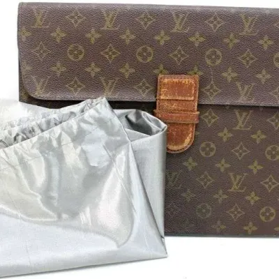 Sale Photo Thumbnail #29: Vintage Louis Vuitton monogram coated canvas portfolio document holder with leather strap closure, showing noticeable wear on the leather tab, accompanied by a silver dust bag.
