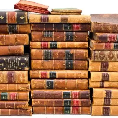 Sale Photo Thumbnail #6: Large collection of antique leather-bound books stacked in three tall columns, featuring gilt detailing on spines and worn covers.