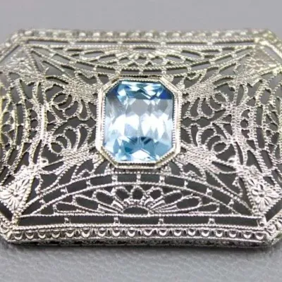 Sale Photo Thumbnail #20: Art Deco white gold or platinum filigree brooch featuring an emerald-cut light blue stone centerpiece, circa 1920s.