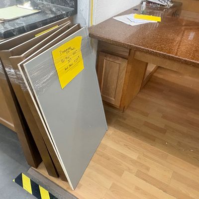 Sale Photo Thumbnail #56: Stack of cabinetry dishwasher end panels leaning against a display unit, tagged with yellow price signs.