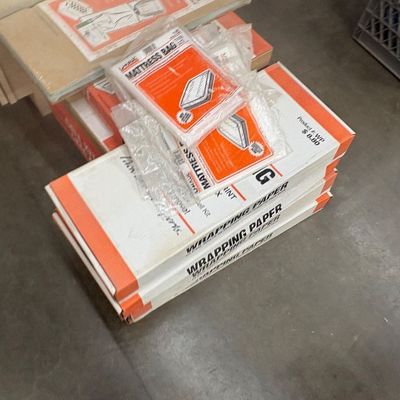 Sale Photo Thumbnail #57: Stack of U-Haul moving supplies, including boxes of wrapping paper and packaged mattress bags.