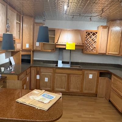 Sale Photo Thumbnail #55: Complete set of modern solid oak kitchen cabinets with dark granite countertops, wine rack, range hood, and two black pendant lights.