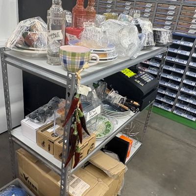 Sale Photo Thumbnail #61: Metal utility shelving unit holding various wrapped housewares, dishes, glassware, and small electronics.