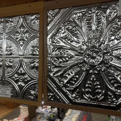 Sale Photo Thumbnail #33: Two framed Victorian-style tin ceiling tile samples featuring intricate embossed floral and medallion patterns with a polished silver-tone finish.