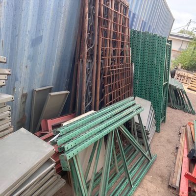 Sale Photo Thumbnail #48: Assorted industrial metal shelving components, rack uprights, crossbeams, and wrought iron gate sections stacked outdoors.