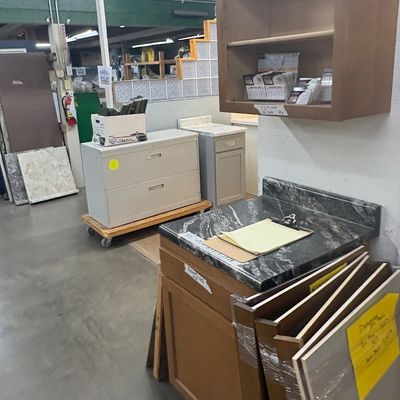 Sale Photo Thumbnail #59: Selection of kitchen and office cabinetry, including a wooden vanity with a dark marble-patterned countertop, wall shelf, filing cabinet, and building materials.