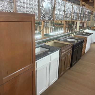 Sale Photo Thumbnail #40: Collection of modern bathroom vanity cabinets in various finishes, paired with granite counters and under-mount sinks, displayed alongside stamped tin ceiling tile samples.