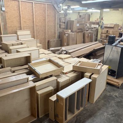 Sale Photo Thumbnail #86: Large assortment of unfinished wooden cabinet drawers, components, and boxed materials in a warehouse setting.