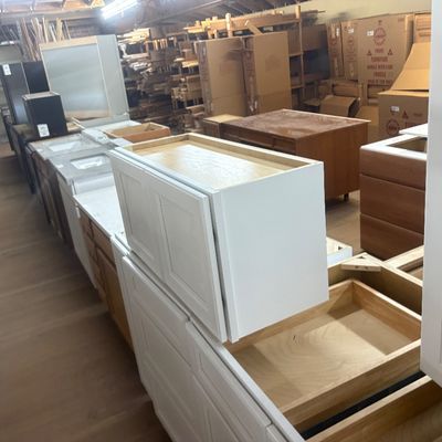 Sale Photo Thumbnail #41: Assortment of modern unfinished and white painted wooden kitchen cabinets, bathroom vanities, and office desks stored in a warehouse setting.