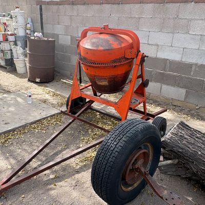 Sale Photo Thumbnail #43: Vintage bright orange portable cement mixer mounted on a towable wheeled frame, showing heavy wear and surface rust from use.