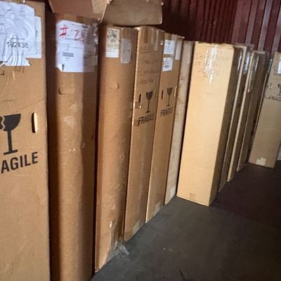 Sale Photo Thumbnail #52: A collection of tall cardboard shipping boxes marked fragile, lined up inside a storage container or warehouse.