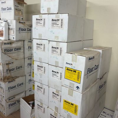 Sale Photo Thumbnail #31: Large stack of sealed cardboard cases containing Bona brand floor cleaning products, labeled with individual prices.