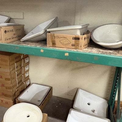 Sale Photo Thumbnail #84: Collection of white ceramic undermount and drop-in bathroom sinks, some in original Hive brand boxes, stored on industrial shelving.