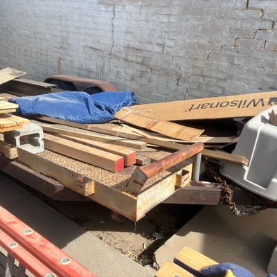 Sale Photo Thumbnail #50: Flatbed utility trailer loaded with assorted construction materials, including scrap lumber, cinder blocks, a Wilsonart box, and a blue tarp.
