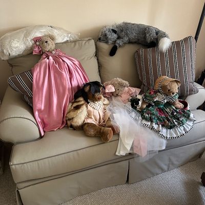 Sale Photo Thumbnail #72: Collection of dressed vintage teddy bears and plush animals arranged on a beige upholstered loveseat, featuring elaborate gowns, bonnets, and faux fur accents.