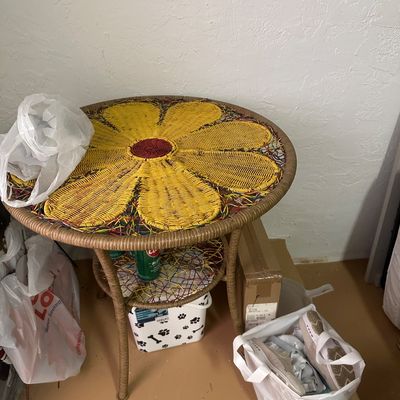Sale Photo Thumbnail #29: Round wicker side table featuring a yellow and red woven flower design top and a lower shelf.