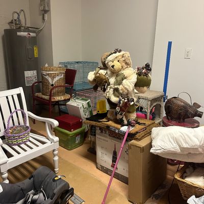 Sale Photo Thumbnail #24: A collection of household goods including a large plush teddy bear figure, a white slat-back armchair, a Graco infant car seat, and various storage items in a utility room setting.