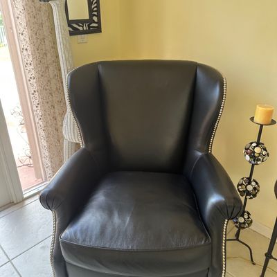 Sale Photo Thumbnail #12: Black leather wingback armchair featuring nailhead trim detailing along the arms and back, supported by tapered square legs.