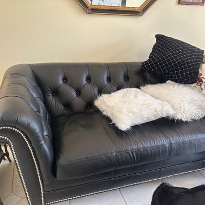 Sale Photo Thumbnail #3: Black leather Chesterfield sofa featuring deep button tufting and silver nailhead trim, styled with throw pillows.