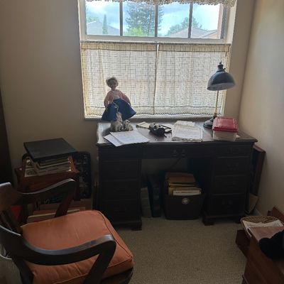 Sale Photo Thumbnail #70: Traditional dark wood pedestal desk with matching office chair, featuring a desk lamp, vintage doll, and miscellaneous paperwork.