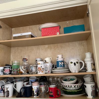 Sale Photo Thumbnail #42: A kitchen cabinet filled with an eclectic assortment of novelty coffee mugs, glassware, ceramic bowls, and small serving pieces.