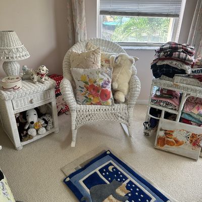 Sale Photo Thumbnail #49: White woven wicker bedroom furniture set including a rocking chair, side table with a matching wicker lamp, and a multi-shelf cart filled with linens.