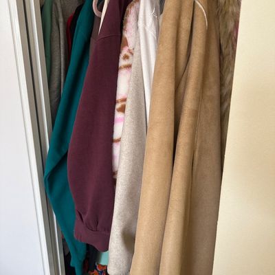 Sale Photo Thumbnail #82: Selection of women's outerwear and sweaters hanging in a closet, including a tan faux suede coat with faux fur trim.