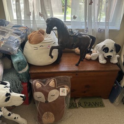 Sale Photo Thumbnail #80: Vintage leather horse statue atop a wooden chest, accompanied by plush toys including a dog and a Squishmallow, along with a packaged Novogratz fox throw pillow.