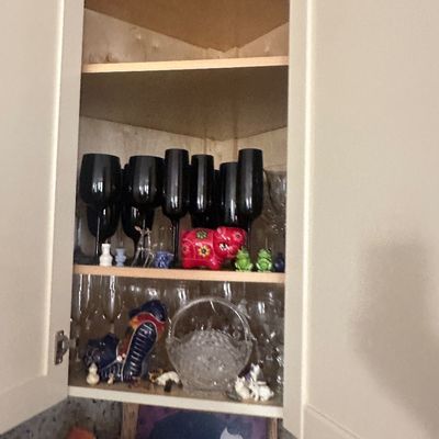 Sale Photo Thumbnail #37: A collection of glassware, including black stems and clear crystal pieces, displayed alongside small ceramic animal figurines in a white kitchen cabinet.