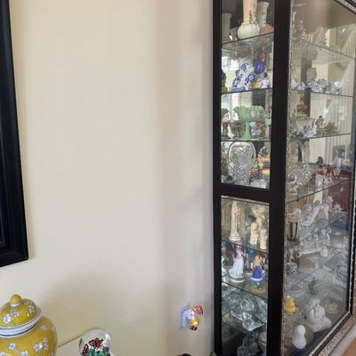 Sale Photo Thumbnail #16: Tall dark wood display cabinet with glass doors and inner lighting, filled with various collectible figurines and glassware.