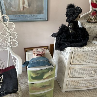 Sale Photo Thumbnail #45: White wicker dresser and matching armchair alongside a framed Pierre-Auguste Renoir art print. A collectible teddy bear in an elaborate black dress and hat sits atop the dresser near a small blue suede belt bag.
