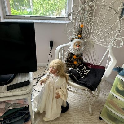 Sale Photo Thumbnail #47: Vintage white painted wicker peacock chair displaying a collectible porcelain clown doll, accompanied by a blonde porcelain doll standing nearby.