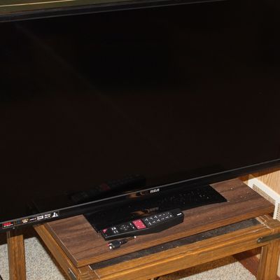 Sale Photo Thumbnail #126: RCA flat-screen television with black bezel, matching remote control, and stand, resting on a small wooden side table.