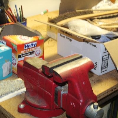 Sale Photo Thumbnail #99: Red heavy-duty bench vise mounted on a wooden workshop table alongside household supplies and tools.