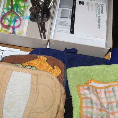 Sale Photo Thumbnail #73: Kitchen drawer filled with miscellaneous household items, including pot holders, cleaning cloths, appliance manuals, and small utensils.