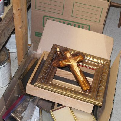 Sale Photo Thumbnail #100: Inlaid wooden crucifix resting inside an ornate gilded picture frame stored in a cardboard box.