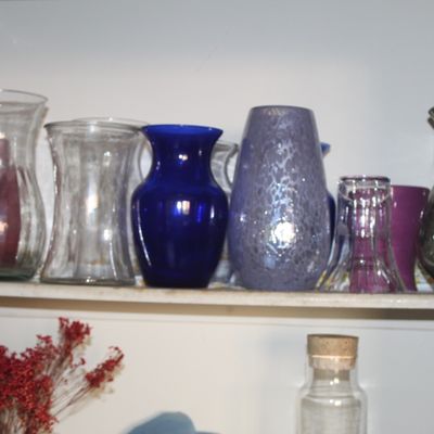 Sale Photo Thumbnail #42: Collection of assorted glass vases, including cobalt blue, mottled lavender, clear glass, and dark smoky gray pieces on a cabinet shelf.