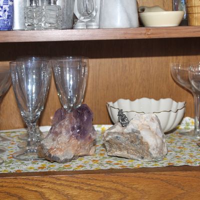 Sale Photo Thumbnail #60: Collection of glassware and decor items displayed inside an oak cabinet shelf, including stemmed goblets, champagne coupes, mineral specimens like an amethyst cluster, and a vintage Mirro kitchen timer.