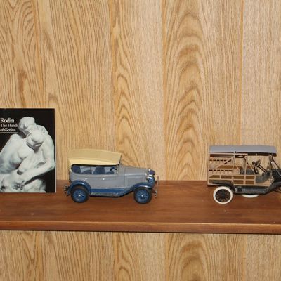 Sale Photo Thumbnail #114: Collection of shelf items featuring vintage die-cast model automobiles, a small Rodin art book, and a partial view of a bronze-style sculpture.