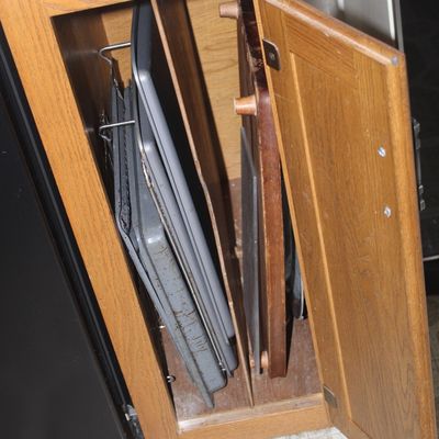 Sale Photo Thumbnail #67: Selection of metal baking sheets, cutting boards, and trays stored vertically inside an oak kitchen cabinet.