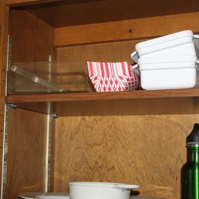 Sale Photo Thumbnail #53: Assorted kitchenware inside a wooden cabinet, including plastic food storage containers, paper food trays, and a green water bottle.