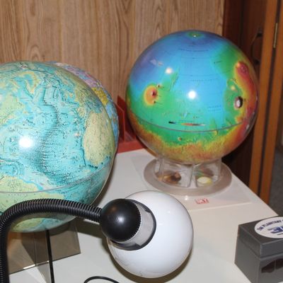 Sale Photo Thumbnail #89: Collection of tabletop educational globes, including a topographical Earth globe and a colorful Mars globe, alongside a small gooseneck desk lamp.