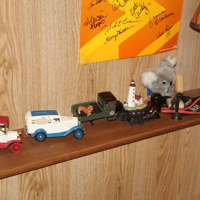 Sale Photo Thumbnail #118: Collection of vintage items including die-cast toy delivery trucks, a small koala plush, a lighthouse figurine, and a personalized wooden lamp base on a shelf.