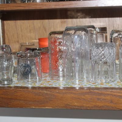 Sale Photo Thumbnail #66: Assorted vintage glassware stored inside a wooden cabinet, including pressed glass tumblers, a glass mason jar, and shot glasses.
