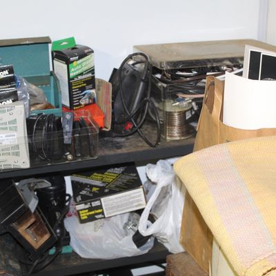 Sale Photo Thumbnail #101: Assorted workshop items and electronics stored on a metal utility shelf, including vintage automotive glass resurfacing kits, power supplies, and various cords.